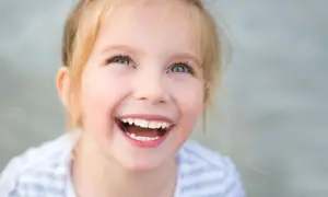 Uśmiechnięta dziewczynka z blond włosami patrzy w górę.