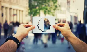 Dłonie trzymają wycięty z papieru profil głowy, z drugiej strony widok miasta.