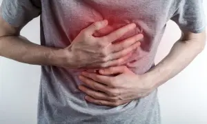 Osoba trzyma się za klatkę piersiową, odczuwając ostry ból. Czerwony obszar na koszulce sugeruje kłucie w klatce piersiowej.