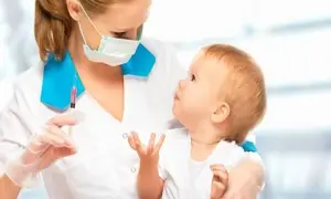 Pielęgniarka w masce trzyma strzykawkę z różowym płynem, patrząc na niemowlę.