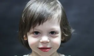 Portret dziecka z niebieskimi oczami i brązowymi włosami na ciemnym tle.