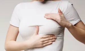 Kobieta w białej koszulce dotyka dłońmi piersi.