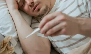 Chory mężczyzna mierzy gorączkę. Objawy mogą przypominać ebolę, ale to tylko grypa.
