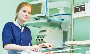 Młody neonatolog zafascynowany pracą przy inkubatorze, otoczony aparaturą medyczną.