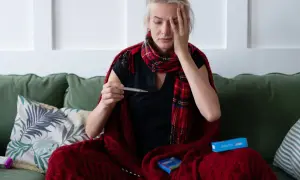 Kobieta z gorączką owinięta kocem trzyma termometr.