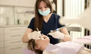 Dentystka w masce i rękawiczkach wykonuje zabieg stomatologiczny u pacjentki.
