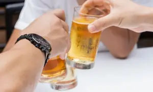 Dłonie unoszące szklanki z piwem do toastu, jedna z nich ma zegarek.