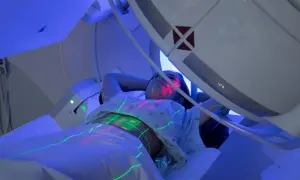 Pacjentka leży pod aparatem do radioterapii, na jej ciele widoczne są zielone i czerwone linie naprowadzające.