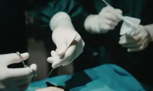 Dłonie chirurga w rękawiczkach trzymające narzędzia chirurgiczne i gazę podczas operacji.