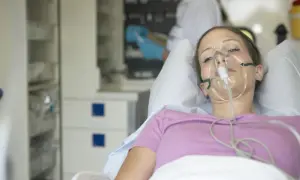Kobieta w masce tlenowej leżąca w łóżku szpitalnym.