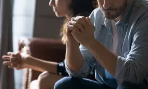 Para siedzi obok siebie, mężczyzna z rękami złożonymi w geście modlitwy, kobieta odwrócona.