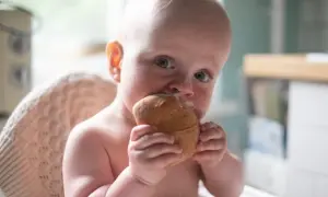 Małe dziecko z zaciekawieniem gryzie bułkę, mimo że może mieć uczulenie na gluten.