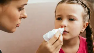 Mama delikatnie przykłada chusteczkę do nosa córki, która ma krew z nosa.