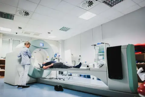 Pacjent leży na stole do badań, a technik przygotowuje się do wykonania scyntygrafii kości.