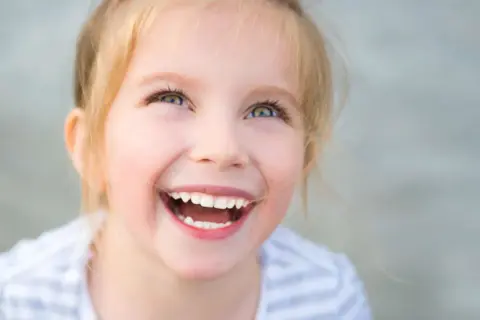 Uśmiechnięta dziewczynka z blond włosami patrzy w górę.