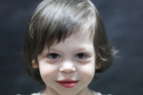 Portret dziecka z niebieskimi oczami i brązowymi włosami na ciemnym tle.