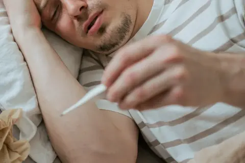 Chory mężczyzna mierzy gorączkę. Objawy mogą przypominać ebolę, ale to tylko grypa.