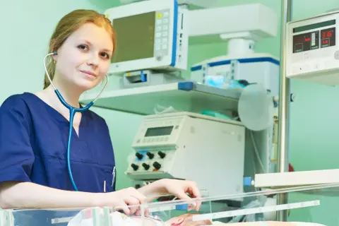 Młody neonatolog zafascynowany pracą przy inkubatorze, otoczony aparaturą medyczną.