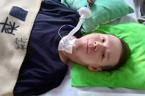 Chłopiec leży w łóżku z rurką tracheostomijną i podłączonym respiratorem.