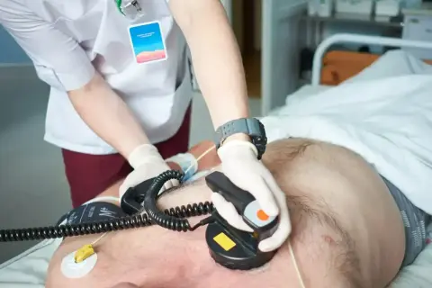 Lekarz wykonuje kardiowersję pacjentowi, przykładając elektrody defibrylatora do klatki piersiowej.