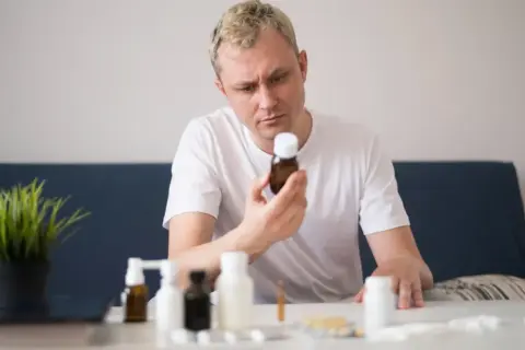 Mężczyzna zastanawia się, czy ashwagandha i alkohol to dobre połączenie. Na stole leżą różne suplementy.