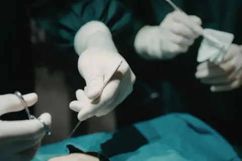 Dłonie chirurga w rękawiczkach trzymające narzędzia chirurgiczne i gazę podczas operacji.