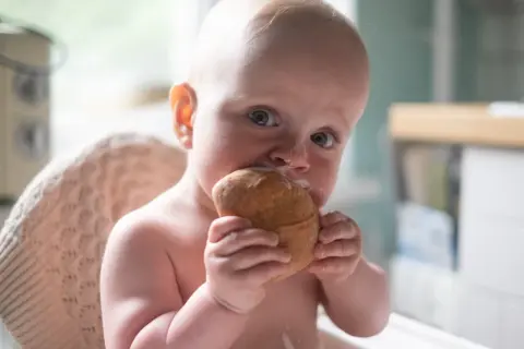 Małe dziecko z zaciekawieniem gryzie bułkę, mimo że może mieć uczulenie na gluten.