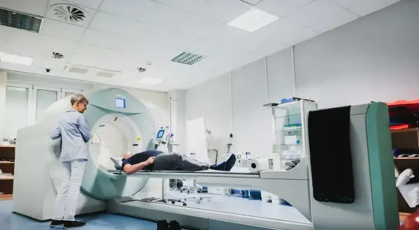 Pacjent leży na stole do badań, a technik przygotowuje się do wykonania scyntygrafii kości.