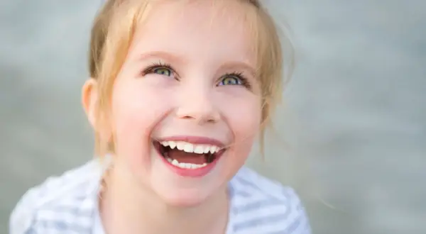 Uśmiechnięta dziewczynka z blond włosami patrzy w górę.