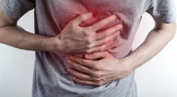 Osoba trzyma się za klatkę piersiową, odczuwając ostry ból. Czerwony obszar na koszulce sugeruje kłucie w klatce piersiowej.