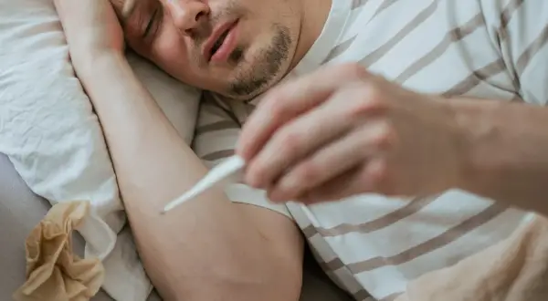 Chory mężczyzna mierzy gorączkę. Objawy mogą przypominać ebolę, ale to tylko grypa.