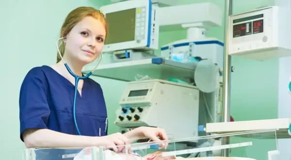 Młody neonatolog zafascynowany pracą przy inkubatorze, otoczony aparaturą medyczną.