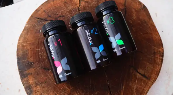 Trzy czarne butelki suplementu thyroset z numerami 1, 2 i 3, ułożone na drewnianej desce.