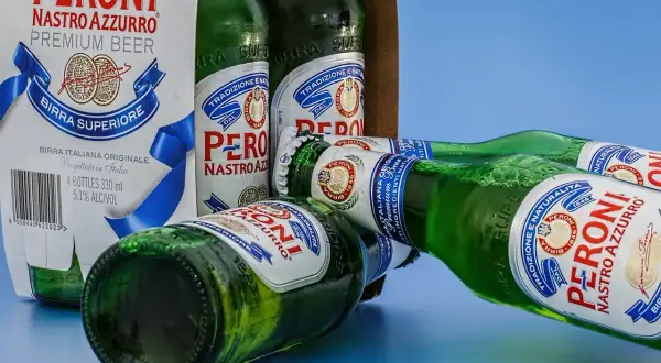 Butelki piwa Peroni Nastro Azzurro leżą obok kartonu. Czy można trzymać alkohol w plastiku? Te butelki są szklane.