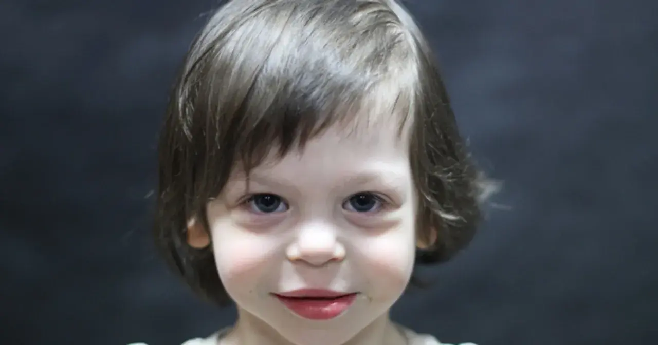 Portret dziecka z niebieskimi oczami i brązowymi włosami na ciemnym tle.
