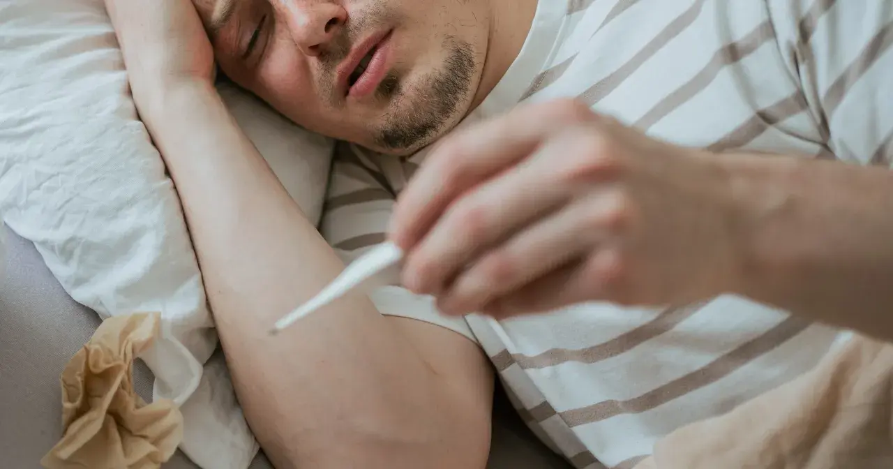 Chory mężczyzna mierzy gorączkę. Objawy mogą przypominać ebolę, ale to tylko grypa.