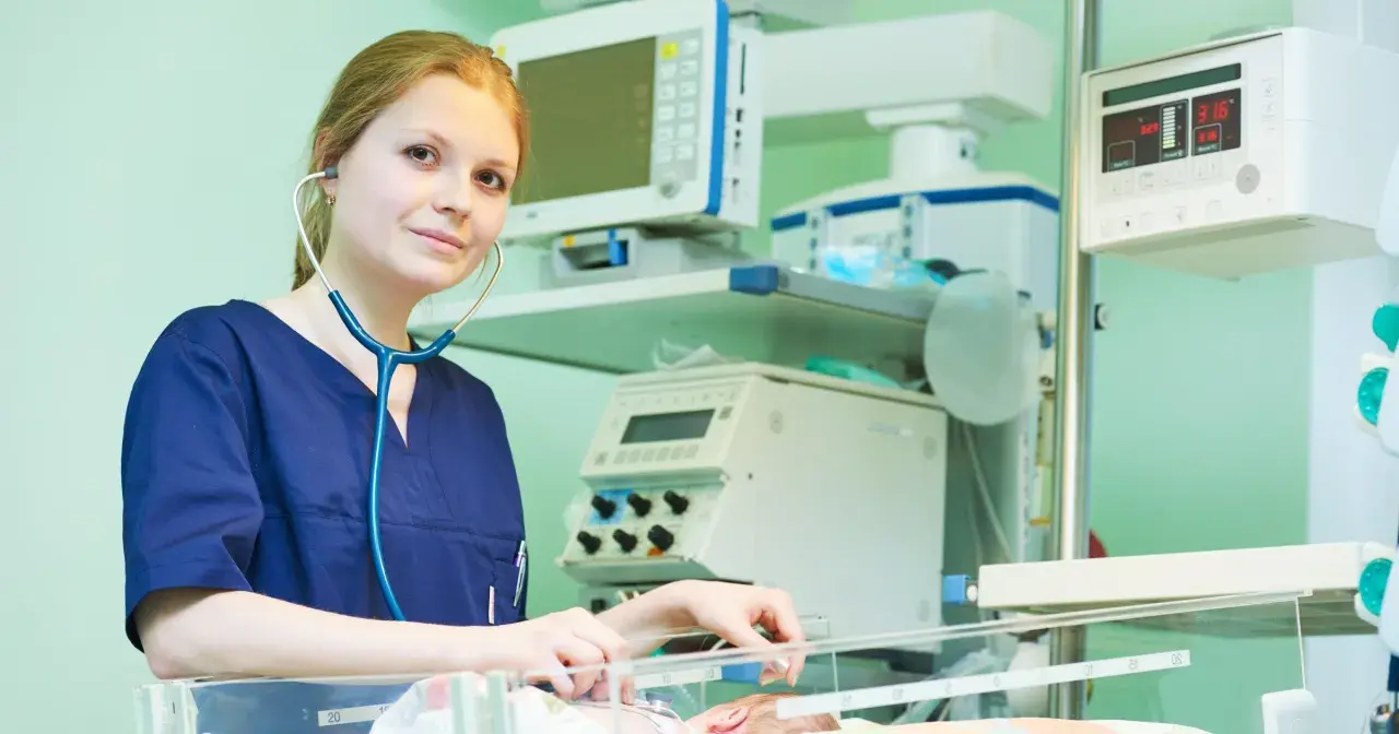 Młody neonatolog zafascynowany pracą przy inkubatorze, otoczony aparaturą medyczną.
