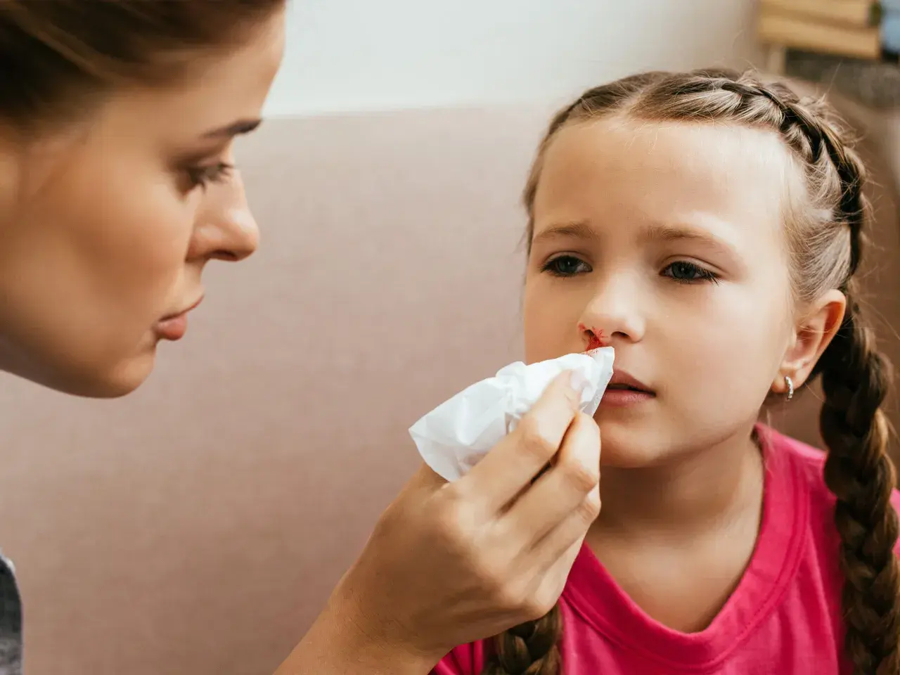 Mama delikatnie przykłada chusteczkę do nosa córki, która ma krew z nosa.
