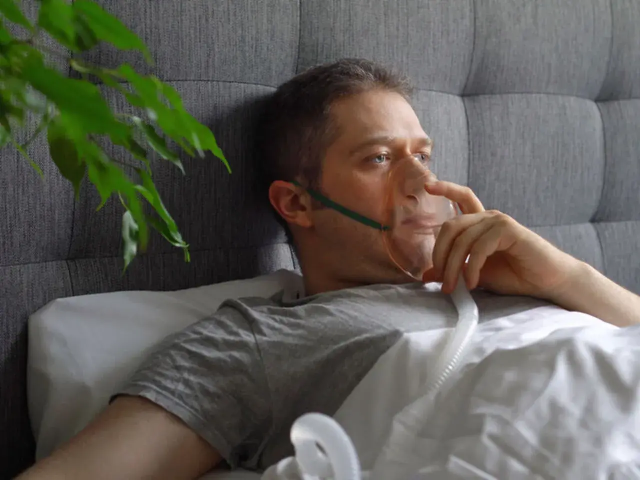 Mężczyzna w masce tlenowej leży w łóżku, podłączony do aparatu do inhalacji.