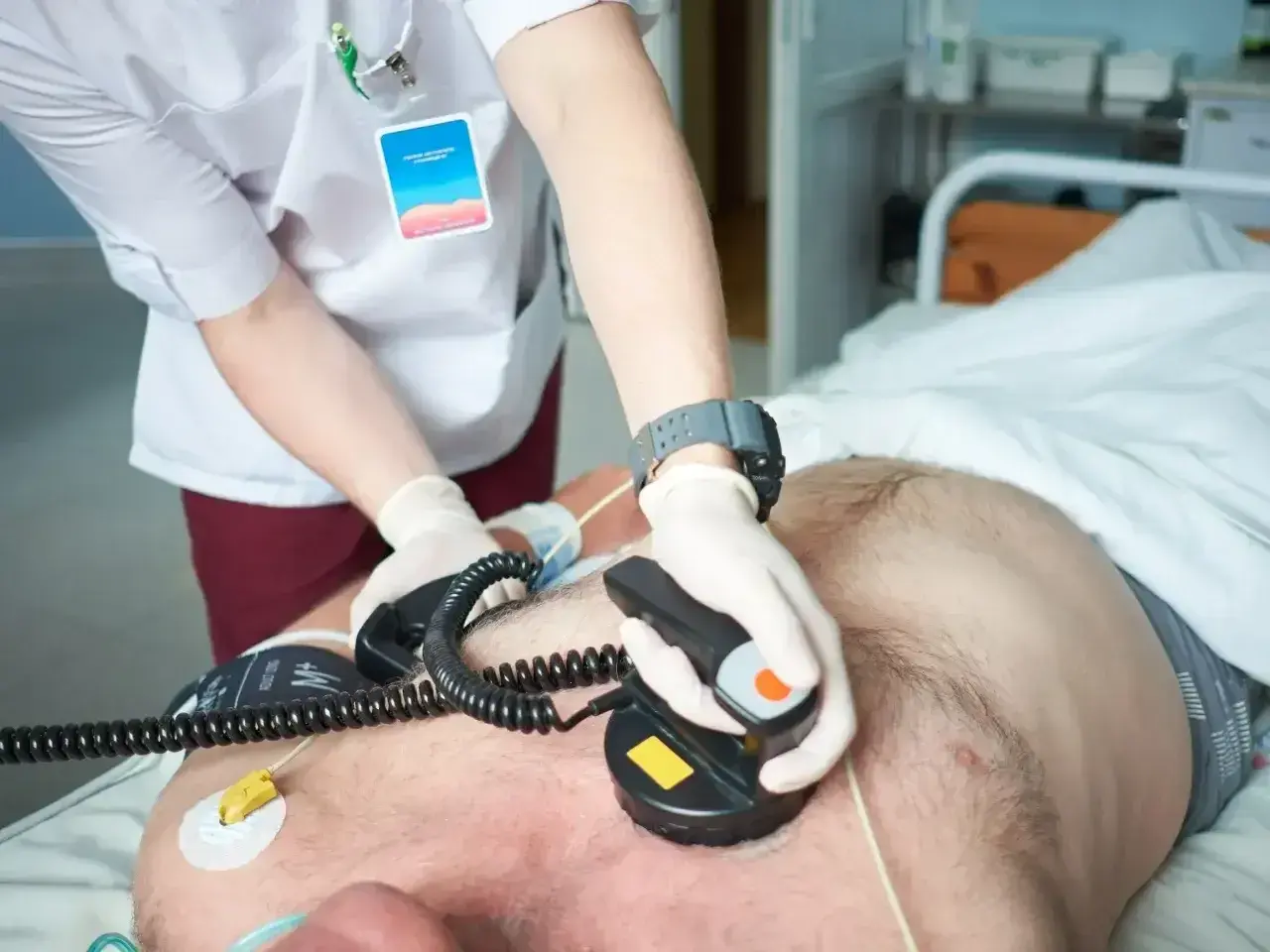 Lekarz wykonuje kardiowersję pacjentowi, przykładając elektrody defibrylatora do klatki piersiowej.