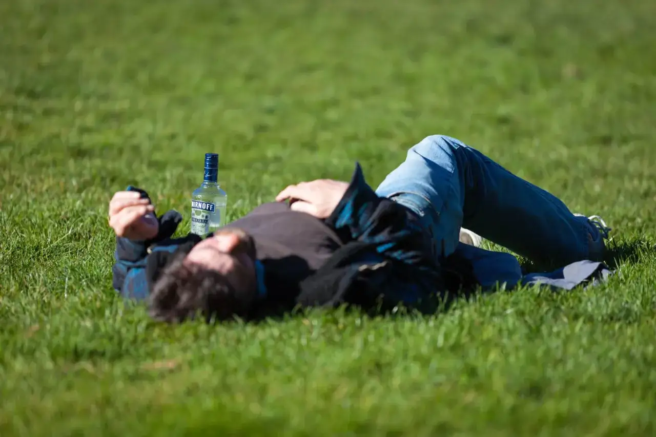 Mężczyzna leży na trawie obok butelki alkoholu. Pytanie: czy można pić alkohol przy padaczce?