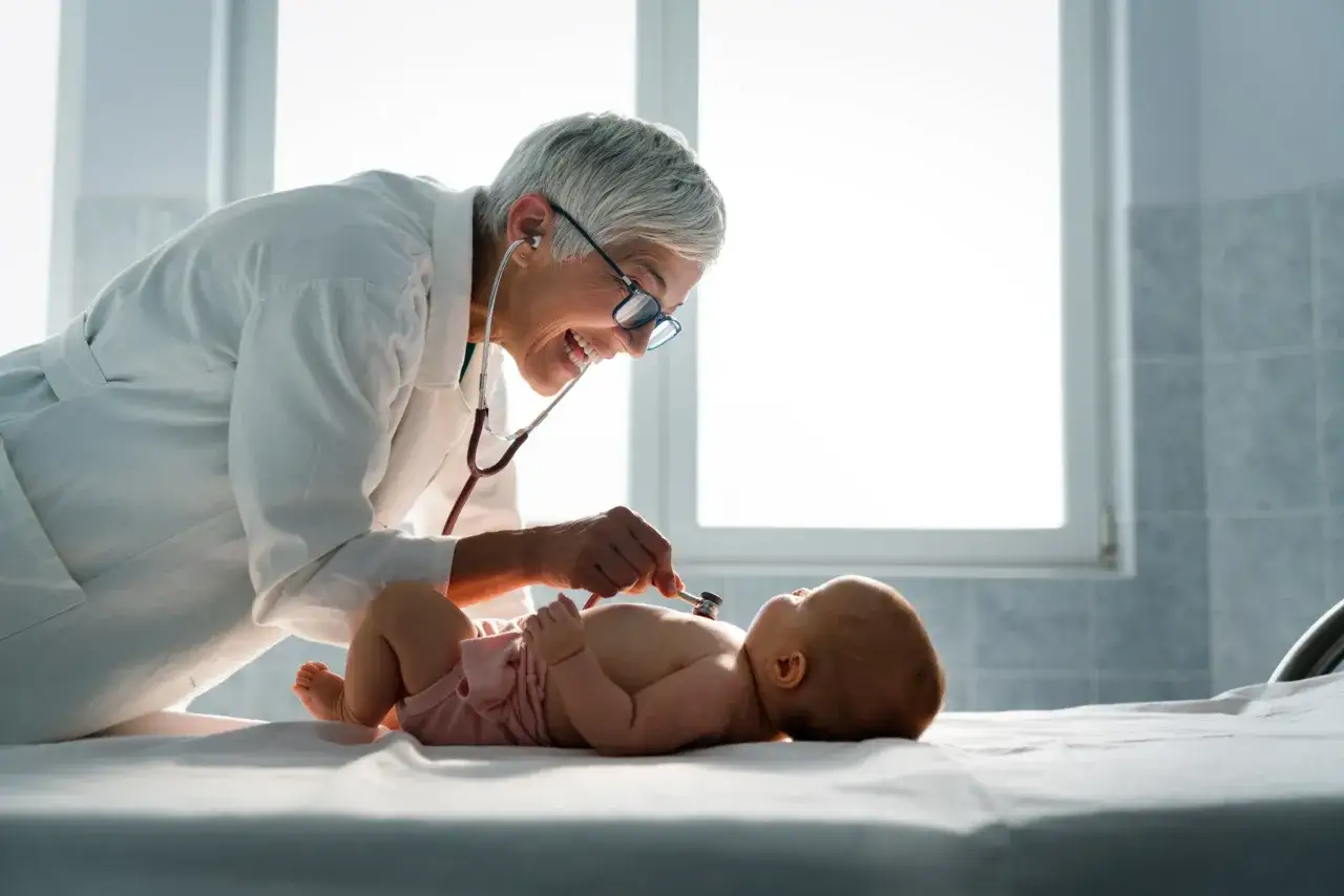 Uśmiechnięty neonatolog bada niemowlę stetoskopem.