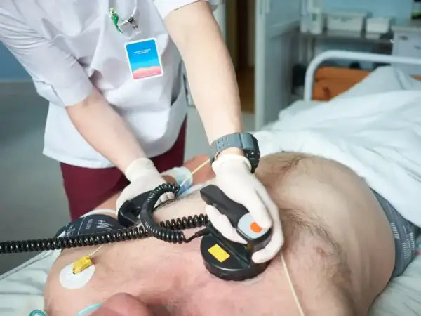 Lekarz wykonuje kardiowersję pacjentowi, przykładając elektrody defibrylatora do klatki piersiowej.